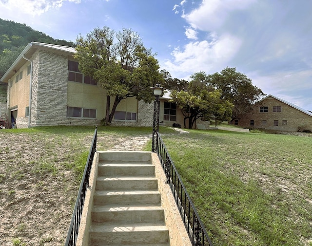 exterior space with stone siding, stairway, and a front yard