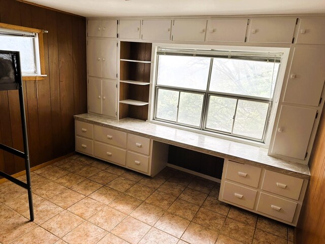 unfurnished office with light tile patterned flooring, built in desk, and wooden walls