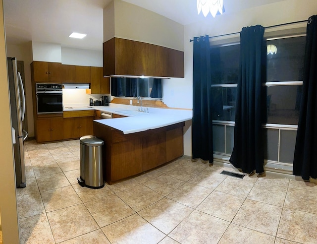 kitchen featuring light tile patterned floors, a peninsula, stainless steel appliances, light countertops, and a sink