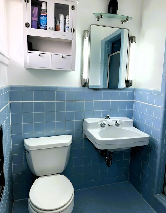 bathroom with toilet, a wainscoted wall, a sink, tile walls, and a shower with door