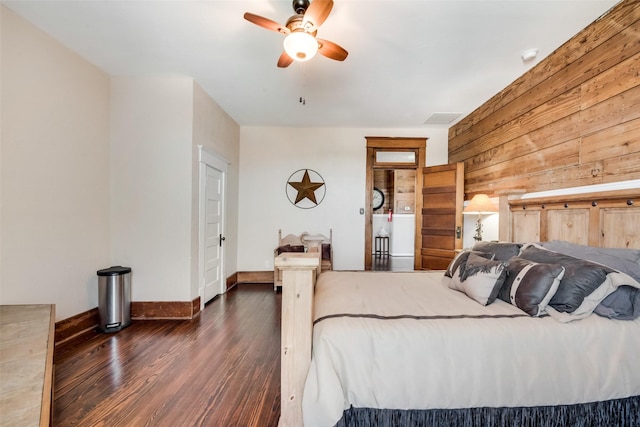 bedroom with ceiling fan, wooden walls, dark wood-type flooring, visible vents, and baseboards