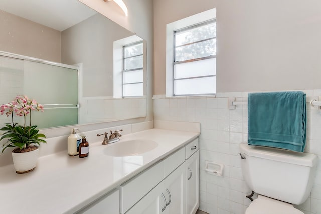 bathroom with vanity, toilet, a shower with shower door, and tile walls