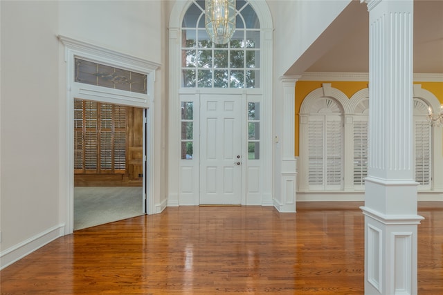 foyer with crown molding, an inviting chandelier, decorative columns, and wood-type flooring