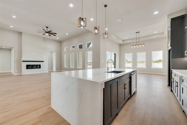 kitchen with ceiling fan, light wood-type flooring, an island with sink, sink, and a fireplace