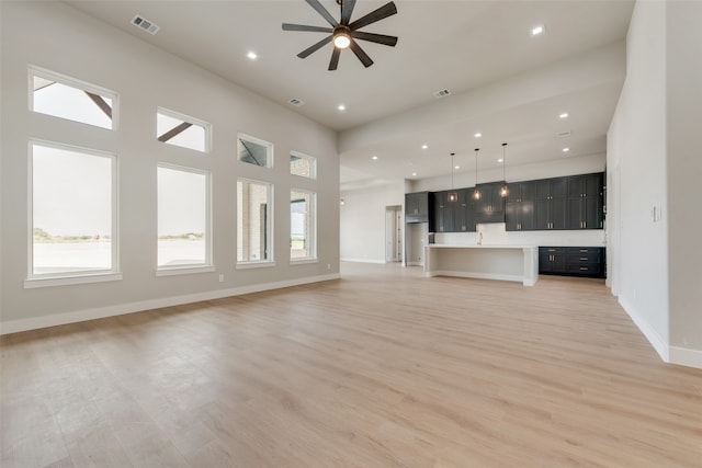 unfurnished living room featuring ceiling fan, light hardwood / wood-style flooring, and a towering ceiling