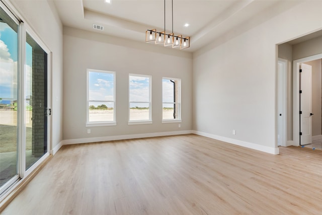 unfurnished room with a raised ceiling, a chandelier, and light wood-type flooring