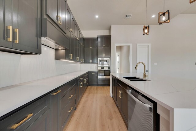 kitchen with backsplash, sink, decorative light fixtures, appliances with stainless steel finishes, and light hardwood / wood-style flooring