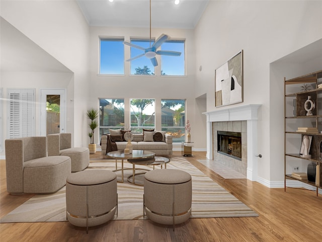 living room with a high ceiling, a tile fireplace, ceiling fan, and light hardwood / wood-style floors