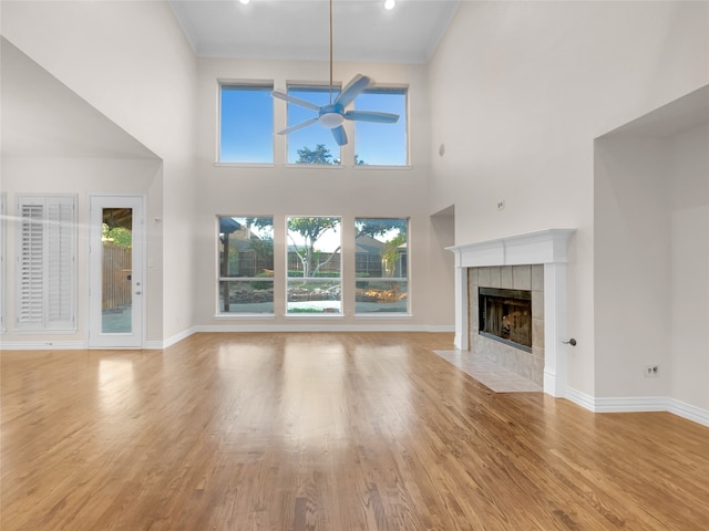 unfurnished living room featuring light hardwood / wood-style floors, a high ceiling, ceiling fan, and a tile fireplace