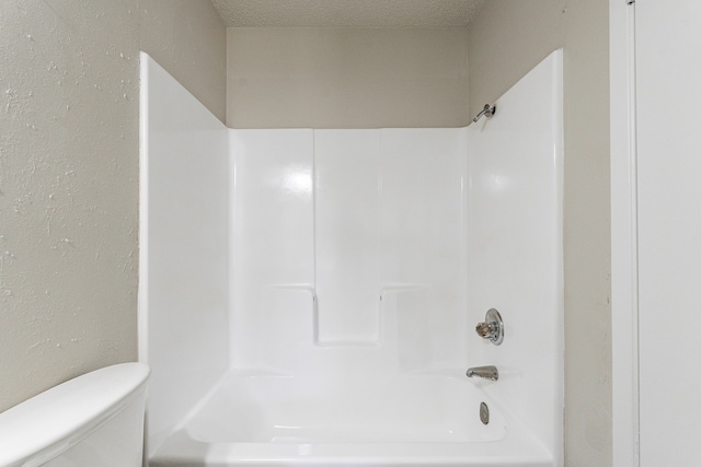 bathroom with washtub / shower combination, toilet, and a textured ceiling