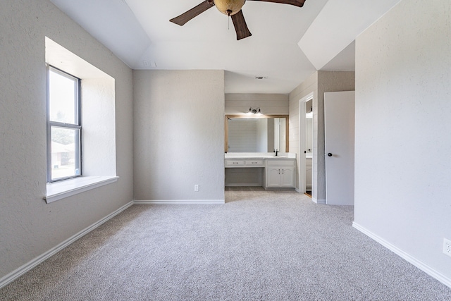 unfurnished bedroom featuring ceiling fan, multiple windows, light colored carpet, and ensuite bath