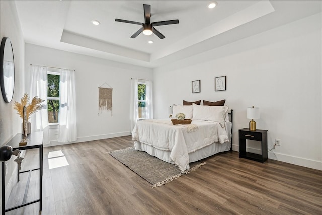 bedroom with dark wood-type flooring, multiple windows, and a tray ceiling