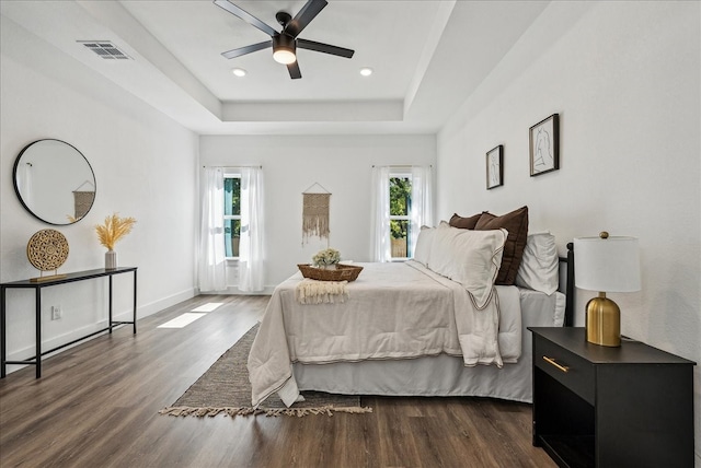 bedroom with ceiling fan, dark hardwood / wood-style floors, and a tray ceiling