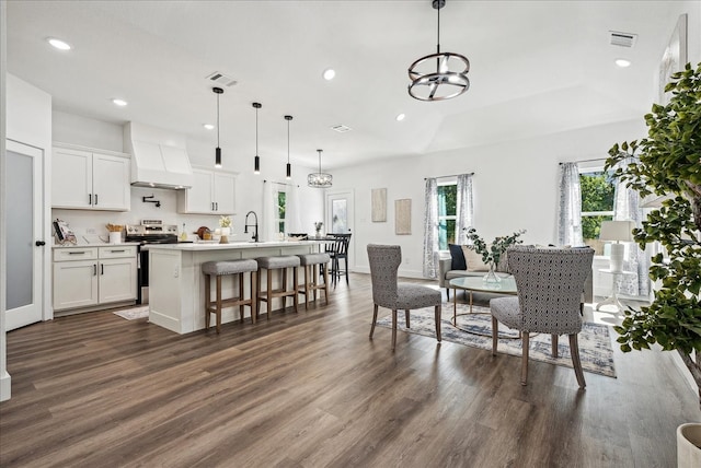 kitchen with stainless steel range with electric stovetop, custom exhaust hood, white cabinetry, dark wood-type flooring, and a center island with sink