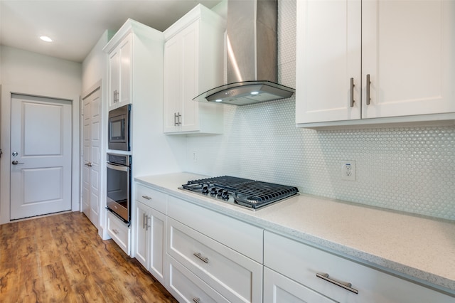 kitchen with backsplash, stainless steel appliances, light hardwood / wood-style floors, white cabinetry, and wall chimney exhaust hood