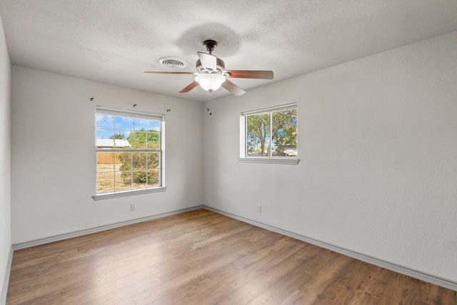 empty room with a textured ceiling, a healthy amount of sunlight, ceiling fan, and wood-type flooring