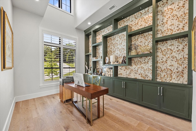 home office featuring built in features, a high ceiling, and light hardwood / wood-style floors