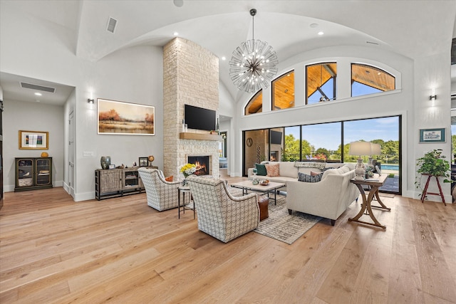 living room featuring brick wall, a fireplace, light hardwood / wood-style flooring, high vaulted ceiling, and a chandelier