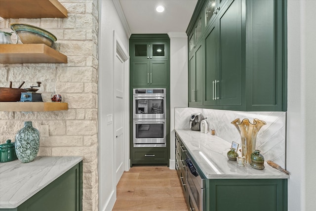 bar featuring green cabinets, stainless steel double oven, light hardwood / wood-style floors, tasteful backsplash, and ornamental molding