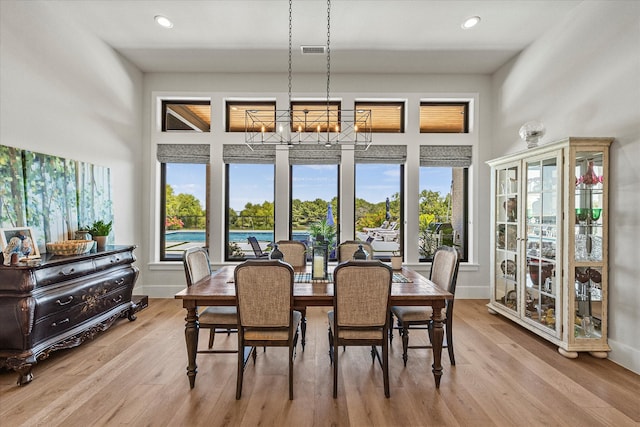 dining area with light wood-type flooring, an inviting chandelier, and a high ceiling