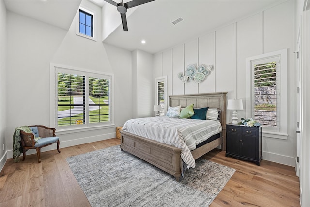 bedroom with light wood-type flooring, multiple windows, ceiling fan, and a towering ceiling