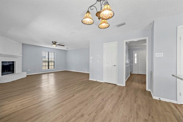 unfurnished living room with a textured ceiling, ceiling fan, wood-type flooring, and a brick fireplace