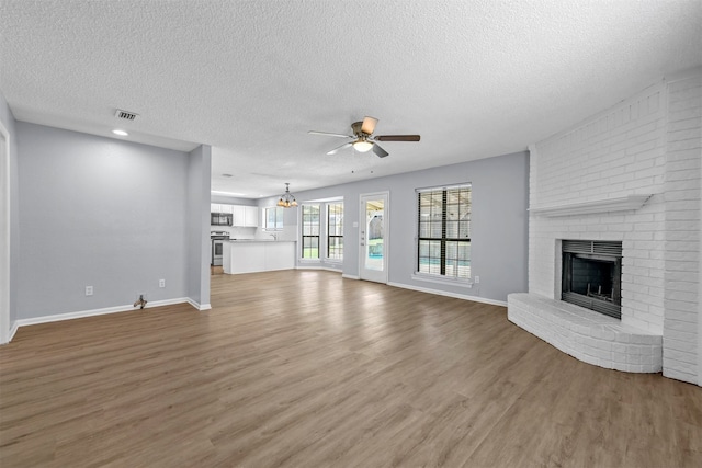 unfurnished living room with a textured ceiling, wood-type flooring, a brick fireplace, and ceiling fan