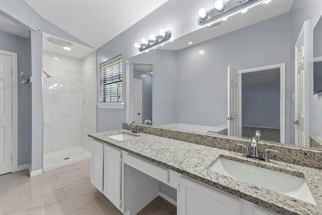 bathroom with a textured ceiling, vanity, tile patterned flooring, and a tile shower