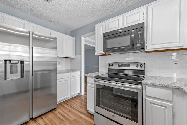 kitchen with light wood-type flooring, appliances with stainless steel finishes, white cabinets, and decorative backsplash