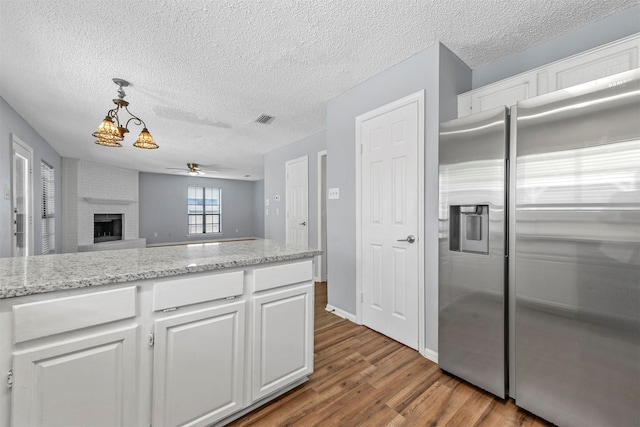 kitchen featuring stainless steel fridge, a brick fireplace, light hardwood / wood-style flooring, and white cabinets