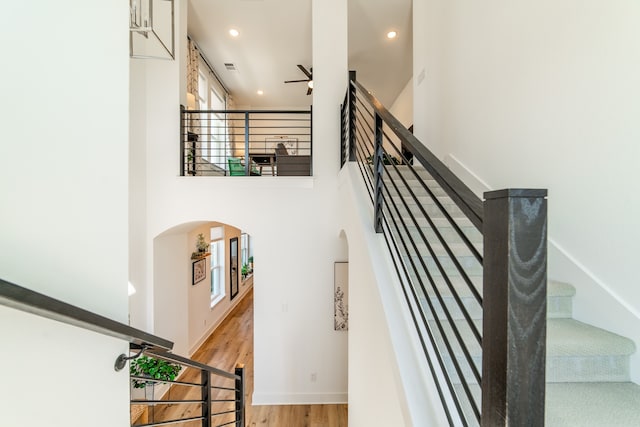 stairs with ceiling fan, wood-type flooring, and a towering ceiling