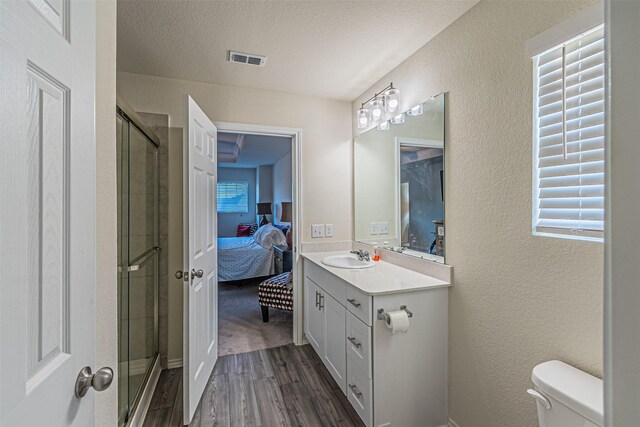 bathroom with a textured ceiling, vanity, an enclosed shower, hardwood / wood-style floors, and toilet