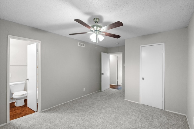 unfurnished bedroom with ensuite bathroom, a closet, carpet, ceiling fan, and a textured ceiling