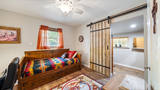 bedroom with a barn door, hardwood / wood-style floors, and ceiling fan