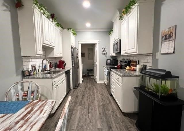 kitchen with appliances with stainless steel finishes, white cabinetry, sink, dark wood-type flooring, and tasteful backsplash