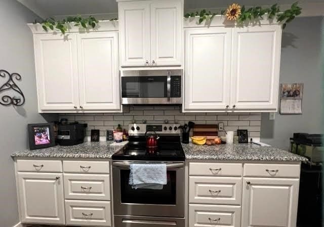 kitchen featuring appliances with stainless steel finishes, light stone counters, decorative backsplash, and white cabinetry