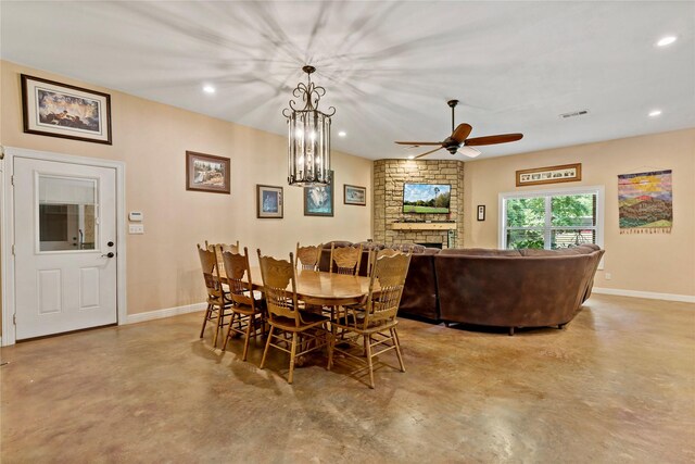 dining area featuring ceiling fan with notable chandelier, a fireplace, concrete floors, and brick wall