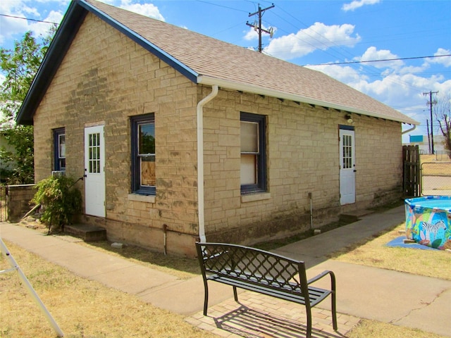 back of property featuring stone siding, roof with shingles, and fence