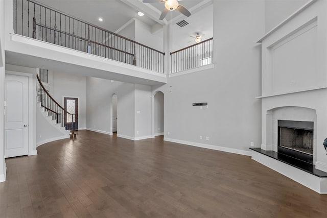 unfurnished living room featuring ceiling fan, a towering ceiling, a tiled fireplace, and dark hardwood / wood-style flooring