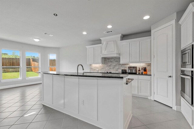 kitchen with appliances with stainless steel finishes, a center island with sink, and white cabinetry