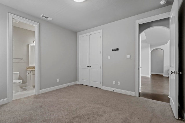 unfurnished bedroom with a closet, ensuite bath, and carpet floors