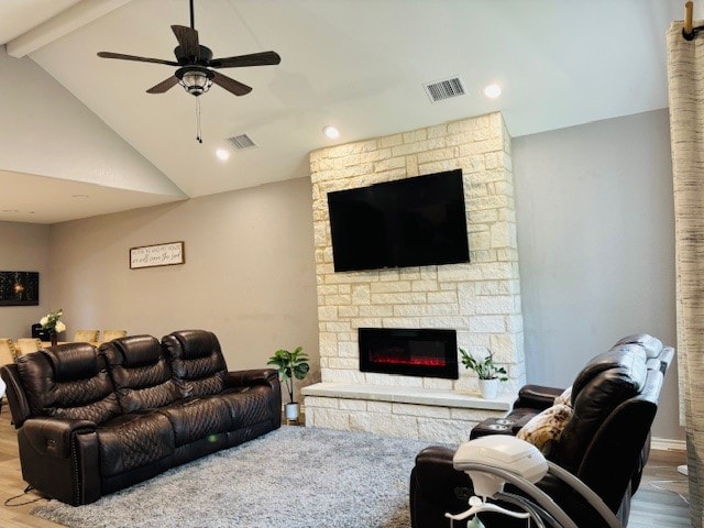 living room with ceiling fan, a stone fireplace, wood-type flooring, and lofted ceiling with beams