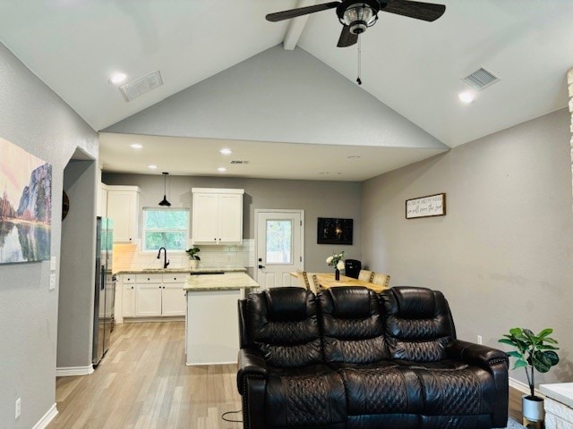 living room with beam ceiling, light hardwood / wood-style floors, sink, high vaulted ceiling, and ceiling fan