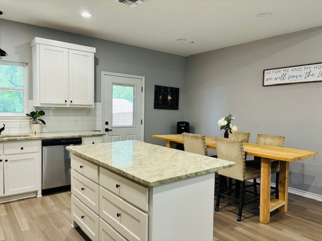 kitchen featuring dishwasher, a center island, light stone countertops, decorative backsplash, and light hardwood / wood-style floors