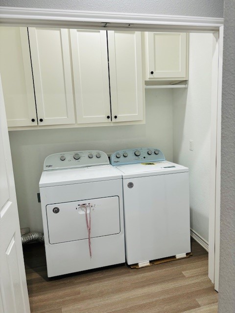 laundry room with washing machine and clothes dryer, cabinets, and light wood-type flooring