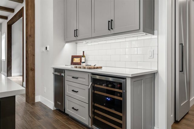 bar with wine cooler, stainless steel fridge, tasteful backsplash, gray cabinetry, and dark wood-type flooring