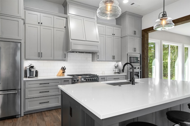 kitchen with gray cabinets, dark hardwood / wood-style floors, sink, a center island with sink, and appliances with stainless steel finishes