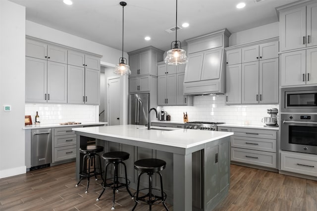 kitchen with an island with sink, dark hardwood / wood-style flooring, stainless steel appliances, decorative light fixtures, and sink