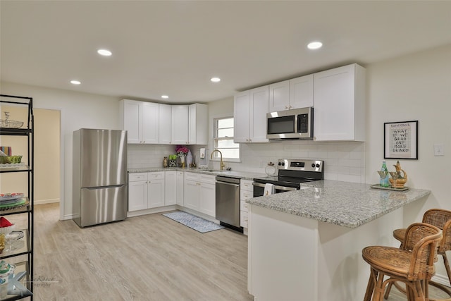 kitchen featuring appliances with stainless steel finishes, white cabinets, light stone countertops, light wood-type flooring, and a peninsula