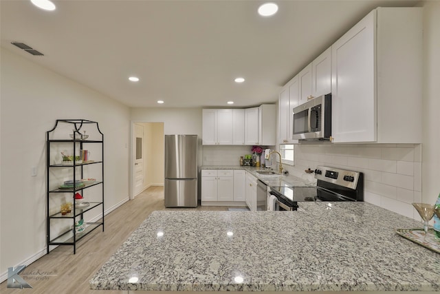 kitchen with white cabinets, light stone countertops, stainless steel appliances, light hardwood / wood-style floors, and sink